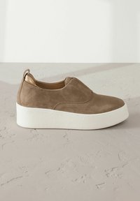 Chaussure à enfiler en daim brun avec une semelle épaisse blanche et une touche métallique dorée au talon. Texture lisse avec un minimum de détails de couture.
