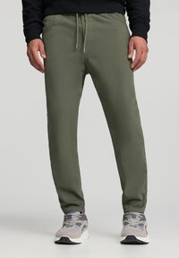 Oliwkowe spodnie dresowe wykonane z lekkiego materiału, posiadające elastyczny pas ze sznurkiem i boczne kieszenie.