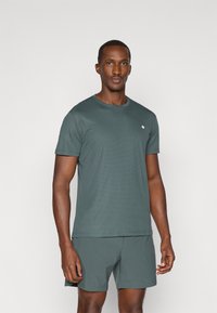 Tumeroheline lühikeste varrukate ja ümmarguse kaelusega t-särk, valmistatud tekstureeritud kangast, millel on rindkere piirkonnas väike logo ja mis on kombineeritud sobivate lühikeste pükste kanssa.