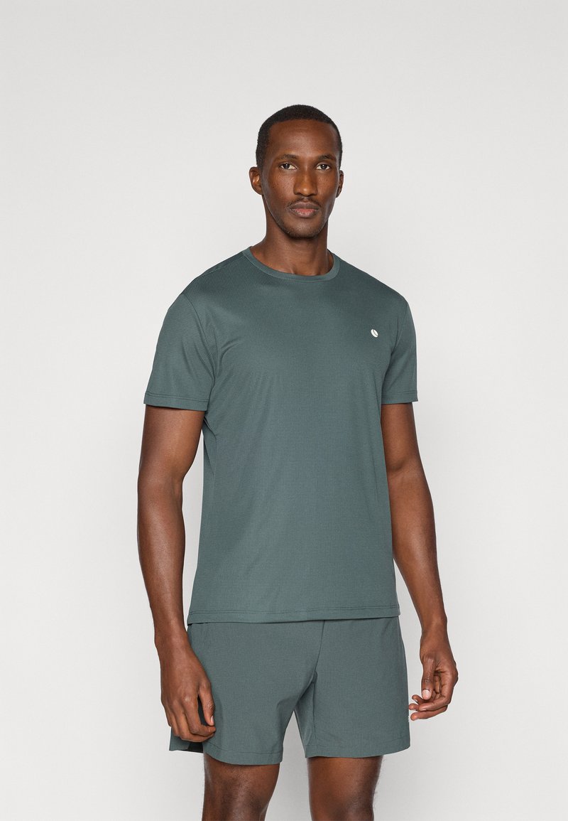 Tumeroheline lühikeste varrukate ja ümmarguse kaelusega t-särk, valmistatud tekstureeritud kangast, millel on rindkere piirkonnas väike logo ja mis on kombineeritud sobivate lühikeste pükste kanssa.