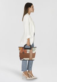 Sac fourre-tout multicolore avec une poignée noire, présentant un design en patchwork et une touche en cuir. Comprend un charme décoratif.