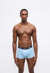 Boxer azzurro chiaro con una cintura nera recante il nome del marchio "HUGO". Il tessuto è liscio con un design aderente.