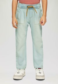 Pantalones de mezclilla azul claro con cintura elástica, cordón y bolsillos frontales; combinados con zapatillas blancas.
