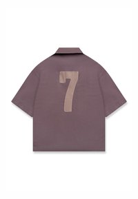Chemise marron à manches courtes avec un écusson beige portant le numéro 7 au dos et un col plat, présentée à plat sur un fond blanc.