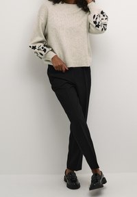 Pull gris clair avec broderie florale noire sur les manches, col rond et poignets côtelés, associé à un pantalon noir et des mocassins brillants.