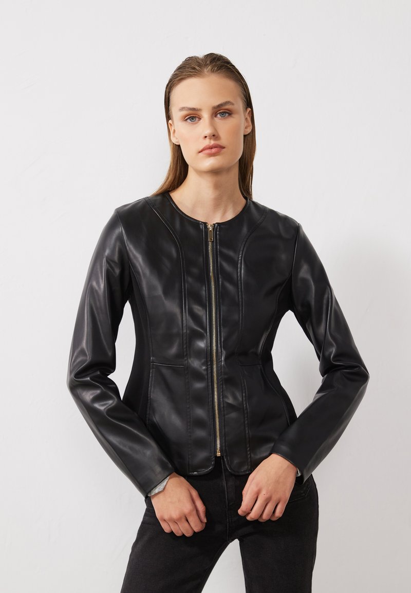 Giacca in ecopelle nera con chiusura tramite zip, collo rotondo e design aderente con dettagli di cucitura sottili. Maniche lunghe e texture liscia.