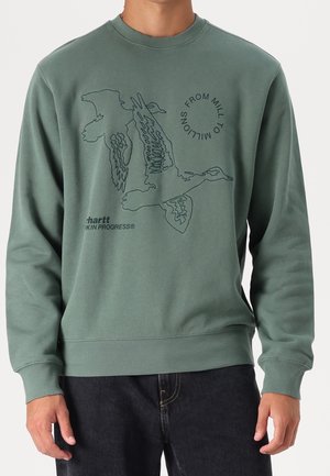 Zielona bluza z czarnym, liniowym rysunkiem lecącej gęsi oraz napisami „FROM MILL TO MILLIONS” i „Carhartt WORK IN PROGRESS” na piersi.