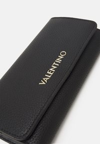 Portofel din piele maro cu un finisaj texturat, având un logo auriu "VALENTINO" pe față și un capac neted îndoit.