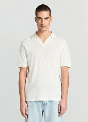 Weißes Poloshirt mit strukturiertem Rautenmuster, kurzen Ärmeln und klassischem Kragen, kombiniert mit hellblauen Jeans.