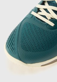 Teal mesh athletic shoe with textured synthetic accents, cream laces, and a white rubber sole, featuring a rounded toe and breathable design.