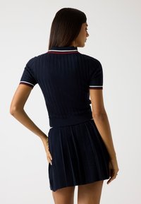 Abito polo a righe navy con maniche corte, gonna a pieghe e accenti di colore a contrasto sul colletto e sui bordi delle maniche.
