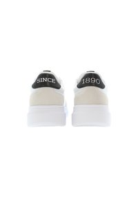 Vita sneakers med en slät ovandel, mockadetaljer och en kraftig vit sula. Svarta hälflikar märkta med "SINCE" och "1890."
