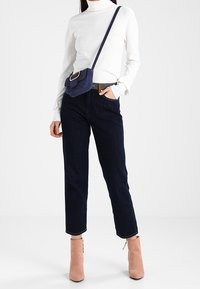 Bílý rolák, tmavé džíny, světle růžové kotníkové boty a námořnická kabelka přes rameno s obdélníkovou sponou.