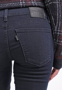 Mörkblå denimjeans med smal passform, med rundade bakfickor och en läderlogotags. Tyget har minimal textur och en slät yta.