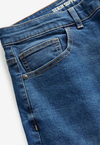 Jeans de mezclilla azul oscuro con corte recto, costuras visibles en color naranja y un bolsillo trasero clásico con detalle de remache.