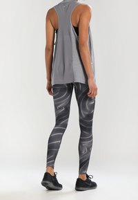 Top deportivo atlético en gris con espalda descubierta, combinado con leggings de patrón blanco y negro que presentan diseños de olas abstractas. Zapatillas negras.