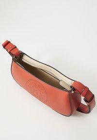 Red leather handbag with a rounded shape, perforated logo detail, and contrasting light beige lining, featuring an adjustable strap and zipper closure.