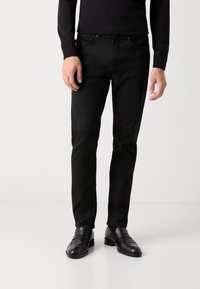 Sorte slim-fit bukser lavet af glat bomuld, der har fem lommer og en lynlås, parret med sorte lædersko.