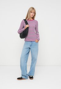 Randig topp med långa ärmar i lila och vitt, kombinerad med ljusblå vida jeans och svarta sneakers. Svart axelremsväska som tillbehör.