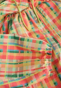 Veste coupe-vent à carreaux colorés avec poignets élastiques, capuche verte à cordon et fermeture éclair sur le devant.