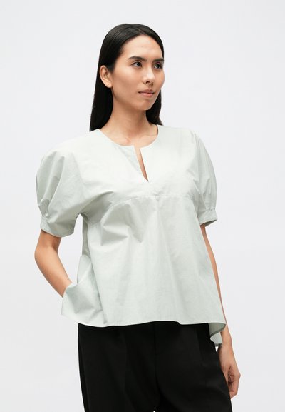Világosszürke rövid ujjú blúz V-nyakkivágással és laza szabással. Puha anyagból készült, enyhén fodros ujjakkal és oldalzsebekkel.
