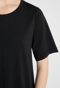 Czarny t-shirt z krótkim rękawem i okrągłym dekoltem. Miękka tkanina o teksturowanej powierzchni, z subtelnymi detalami wzdłuż rękawów i bocznego szwu.