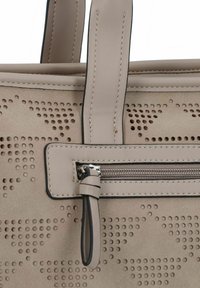 Sac à main en cuir beige avec des perforations semblables à des perles, comportant une poche zippée et des accents cousus sur le bord et les poignées.