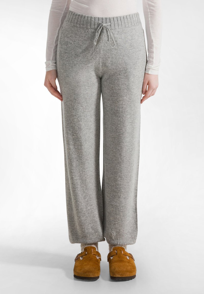 Grijze, gebreide wijde broek met een trekkoord, elastische tailleband en zachte textuur, gecombineerd met bruine suède klompen.