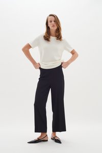 Vit kortärmad topp instoppad i högmidjade svarta vida byxor, tillsammans med svarta platta skor. Enkel, ren design med en slät yta.