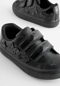 Czarne buty dziecięce z motywem motyli, wykonane z błyszczącego materiału, z dwoma rzepami i teksturowanymi czarnymi gumowymi podeszwami.