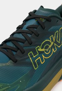 Πετρόλ αθλητικό παπούτσι με μαύρα κορδόνια, υφασμάτινο άνω μέρος με υφή και έντονο κίτρινο λογότυπο. Διαθέτει μαλακή σόλα με ανάγλυφο πέλμα.