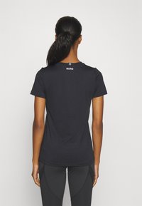 Camiseta negra de manga corta con una textura suave, que presenta un logo en la parte posterior del cuello y un escote redondo. Combinada con leggings negros.