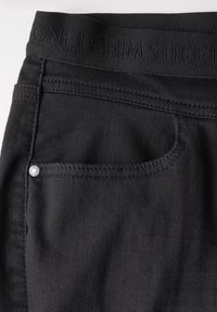 Svarta denimjeans har ett strukturerat tyg med en smal midjeband präglad med "ONE DENIM STREET" och en liten silverdetalj på framfickan.