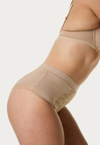 Beige high-waisted ondergoed van een gladde stof met kantafwerking aan de zijkanten. Heeft een naadloos design en zacht, rekbaar materiaal.