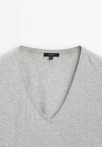 T-shirt grigio a collo a V realizzato in tessuto morbido e leggero. Presenta un collo pulito e cuciture minime con un piccolo etichetta nera nella parte posteriore.