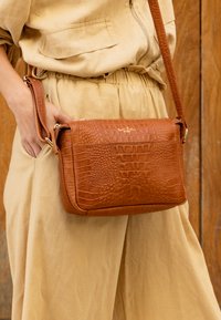 Brązowa skórzana torba na ramię z teksturowanym wzorem krokodyla, z zamknięciem na zamek i złotymi akcentami metalowymi.