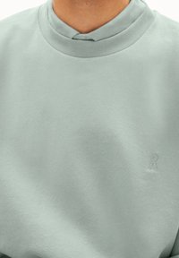 Miellyttävän pehmeä, hillityn vihreä collegepaita, jossa on sileä pinta. Siinä on pyöreä kaulus ja kohokuvioitu logo alakulmassa.