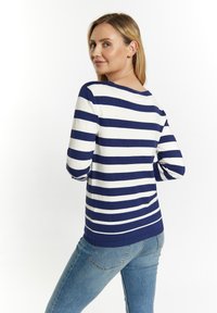 Jūrinis ir baltas dryžuotas megztinis, ilgos rankovės, megztas tekstūra, apvalus iškirpimas, dėvimas su šviesiai mėlynomis džinsomis, pabrėžiantis laisvą siluetą ir nugaros vaizdą.