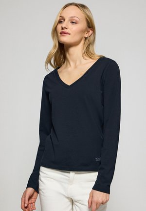 Long-sleeve, navy V-neck top made of soft fabric. Features a fitted silhouette with minimal branding on the lower hem.