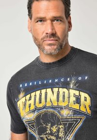 Sort T-shirt med korte ærmer og stort gult "THUNDER" tryk med lynmotiver og et kraniegrafik. Blød tekstur, rund halsudskæring.