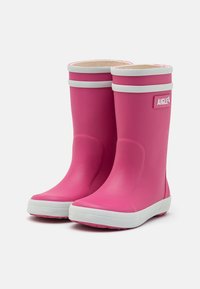 Bottes de pluie en caoutchouc roses avec des accents blancs, présentant une texture lisse et un bout arrondi. Conçues pour offrir une protection imperméable et une durabilité.