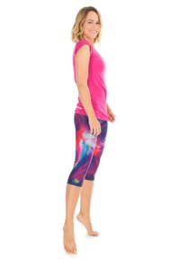 Rosa, figurnära t-shirt och färgglada, mönstrade capri leggings med snurrande nyanser av lila, röd och blå. Barfota, vänd åt vänster.