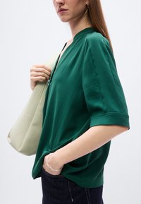 Haut vert à coupe décontractée avec manches courtes, doté d'un col en V et d'une texture douce. Porté avec un sac à épaule de couleur claire.