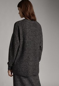 Ciemnoszary sweter dziany o luźnym kroju, z długimi rękawami i prążkowaną fakturą. Ty�ł posiada zaokrąglony dół oraz subtelny wzór.