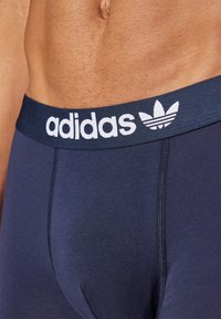Navy blue Adidas boxer briefs feature a soft waistband with white logo and a sleek, smooth texture. Designed for comfort and fit.