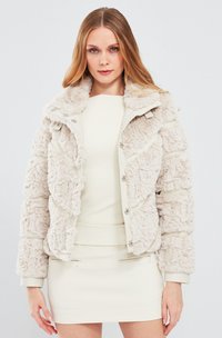 Faux fur jas in lichtbeige met een puffy textuur, knoopsluiting en een zachte kraag. Bevat verticale gequiltte accenten en manchetten.