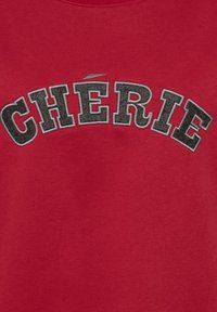 Rode sweatshirt met het woord "CHERIE" in vetgedrukte, versleten zwarte letters. Zacht katoen met een klassieke ronde hals.