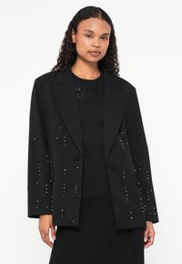 Blazer nero con design sartoriale, caratterizzato da accenti di strass sparsi. Realizzato in un tessuto liscio con una vestibilità strutturata e colletto a revers.