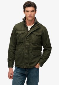 Veste verte et légère avec quatre poches avant, boutons-pression et un col à carreaux ; fabriquée en tissu durable avec une finition légèrement texturée.