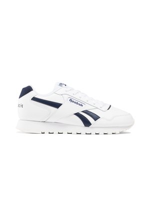 Baskets Reebok blanches avec des rayures bleu marine, une semelle basse et des lacets, présentées en profil droit sur un fond blanc.